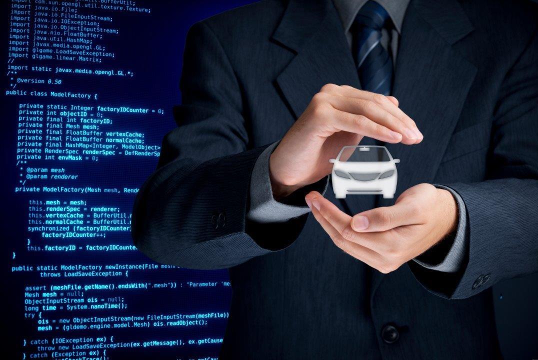 Person in a suit holding a small car model with code displayed on a screen in the background, symbolizing technology in the automotive industry.
