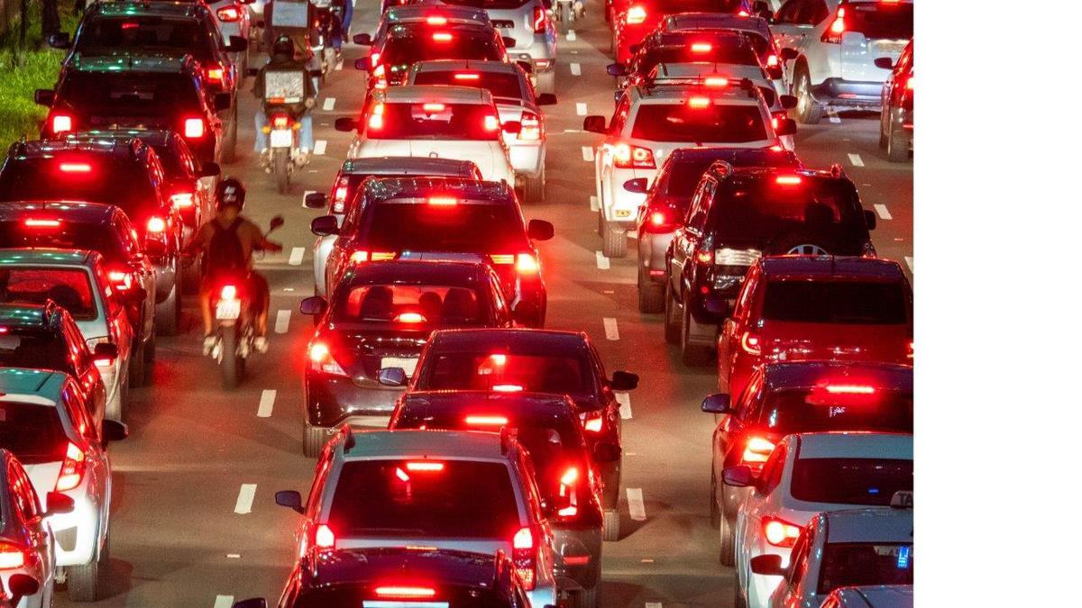 Heavy traffic on a multi-lane road at night, with numerous cars and motorcycles, all with illuminated red brake lights.