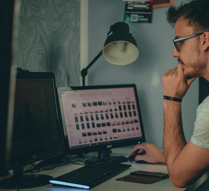 A man with glasses contemplates images on computer screens with multiple thumbnails depicting Storyblok website development.